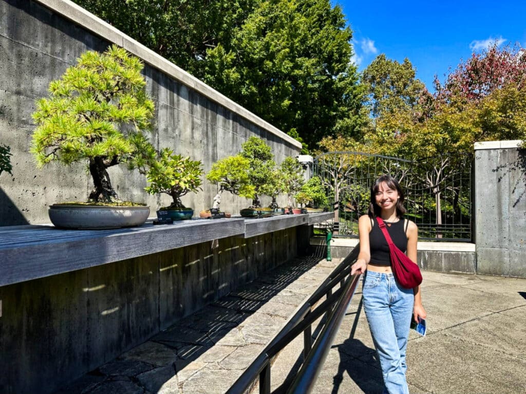 The author Lea Rose Allbaugh, posing for a photo near the displayed bonsais at North Carolina Arboretum