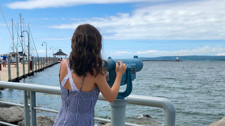 A woman gazes through binoculars, intently observing the water in front of her.