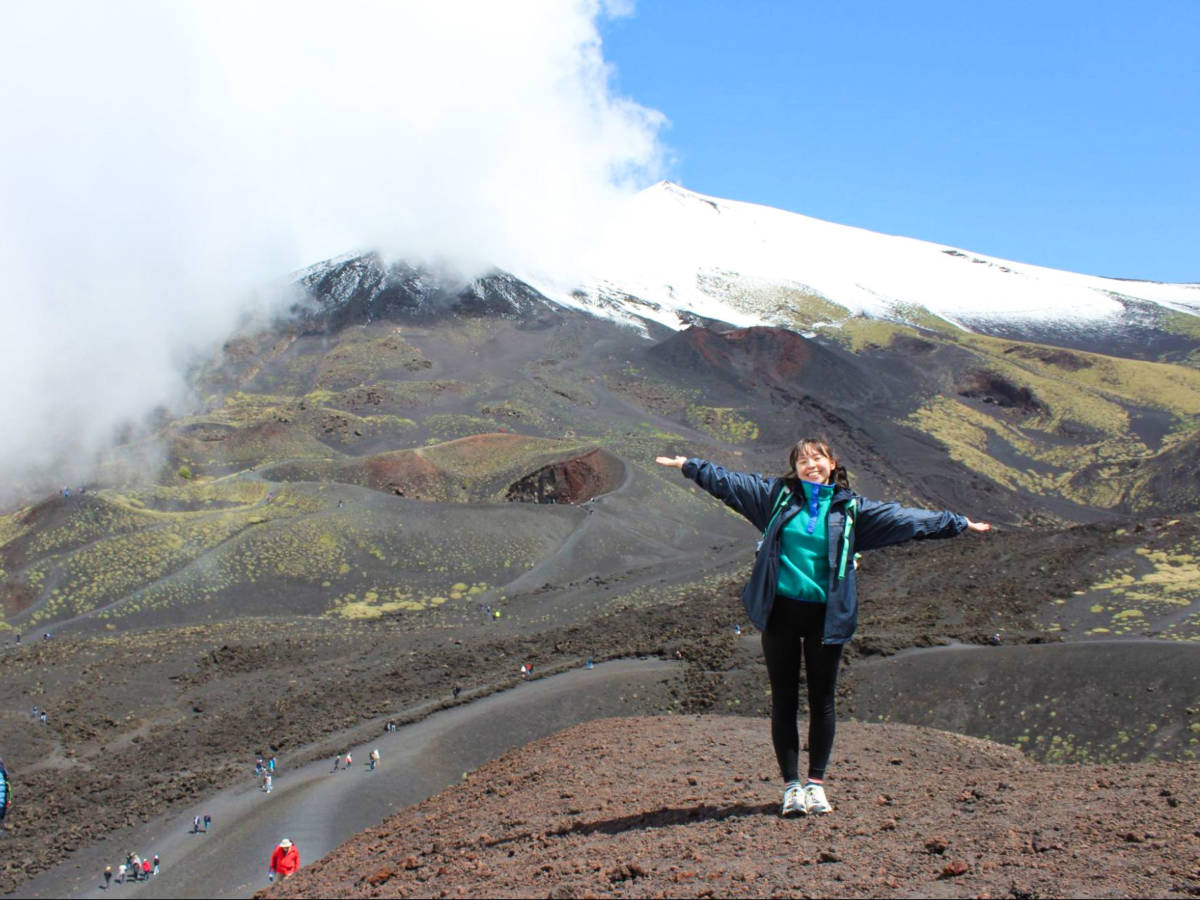 The author Lea Rose Allbaugh, posing for a photo with the Mount Etna in the background