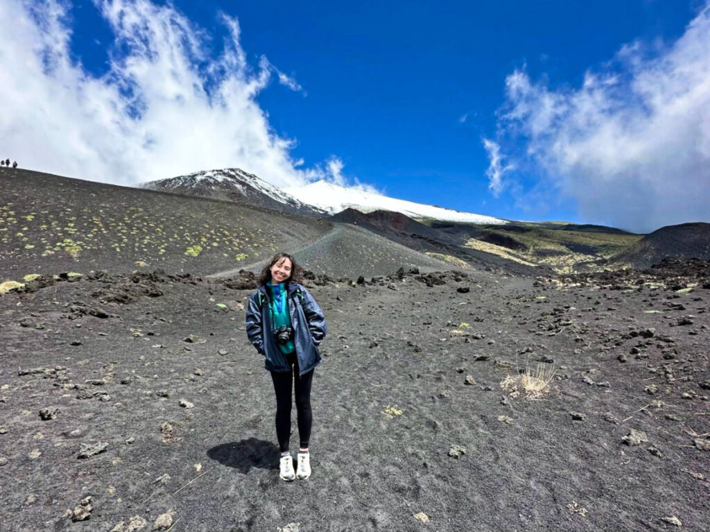 The author Lea Rose Allbaugh, smiling for a photo with the Mount Etna in the background