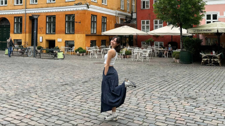 The author Lea Rose Allbaugh, posing for a photo in the middle of the street with colorful buildings around Copenhagen, Denmark