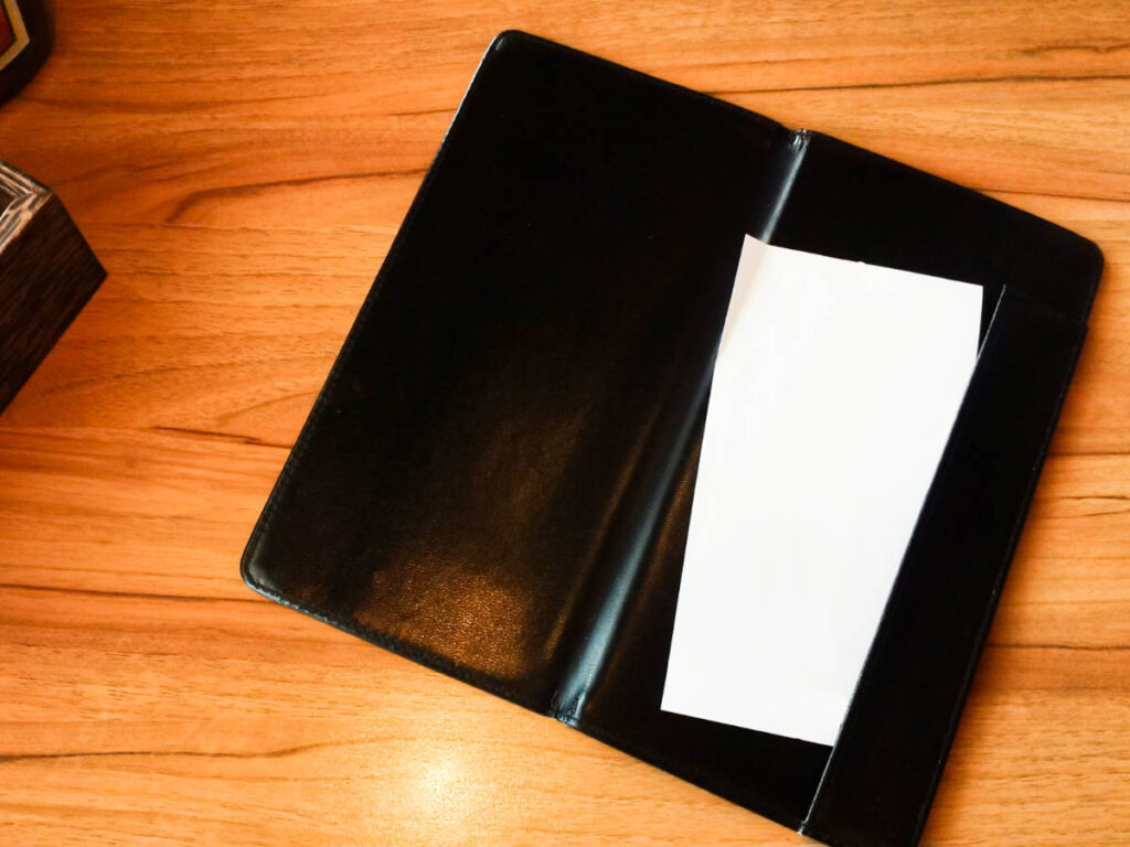 A leather restaurant bill holder with a blank receipt on the wooden table