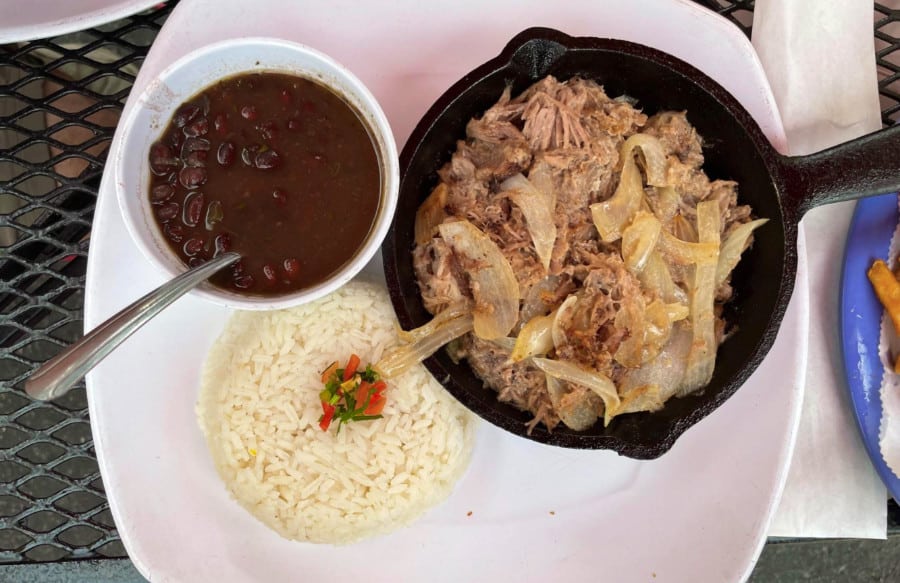 A plate with a small pan full of lechon or sauteed roasted pork, black bean sauce in a bowl and rice