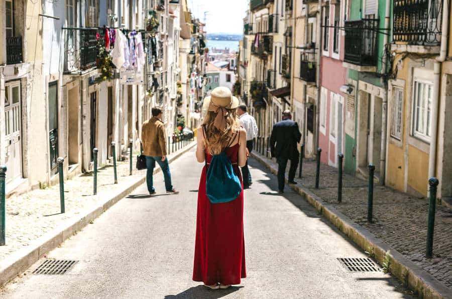A young woman in red dress standing in the middle of the cozy street of Lisbon with tourists around