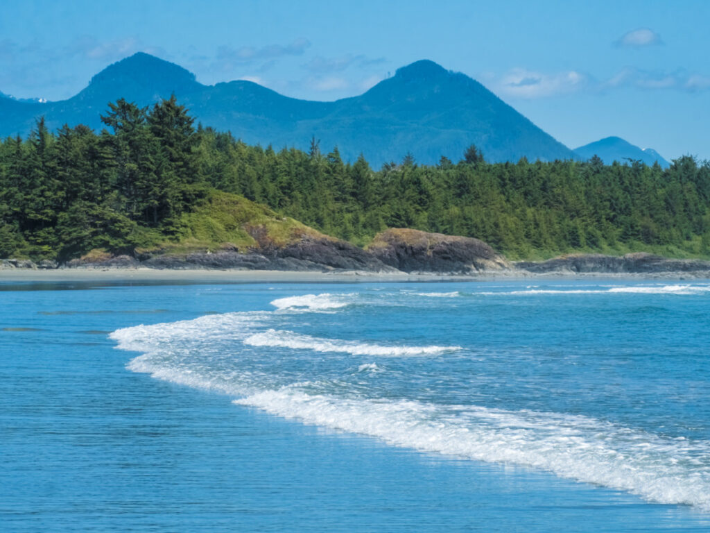 A scenic beach with rolling waves and majestic mountains in the background at Pacific Rim National Park Reserve