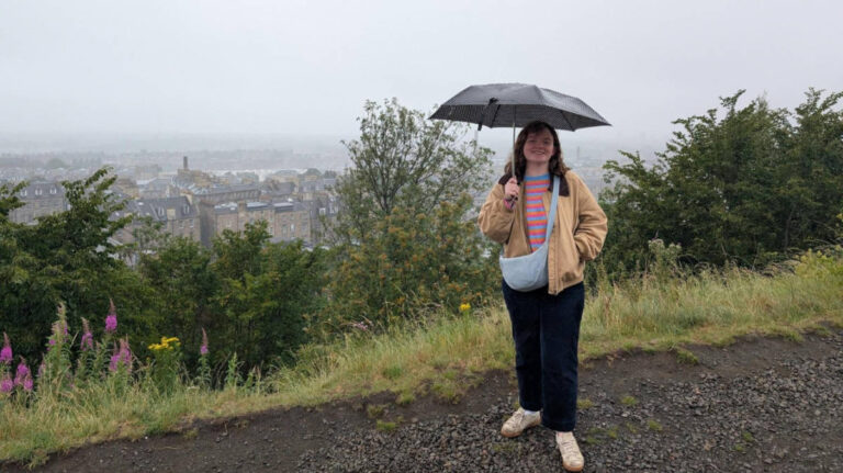 The author Louise Wylie holding an umbrella at the overlooking viewpoint of Leith on a rainy day