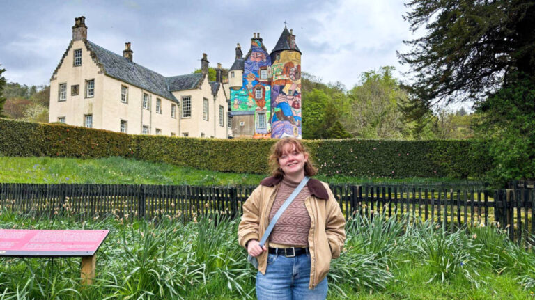 The author Louise Wylie posing for a photo in front of the colorful towers of Kelburn Castle