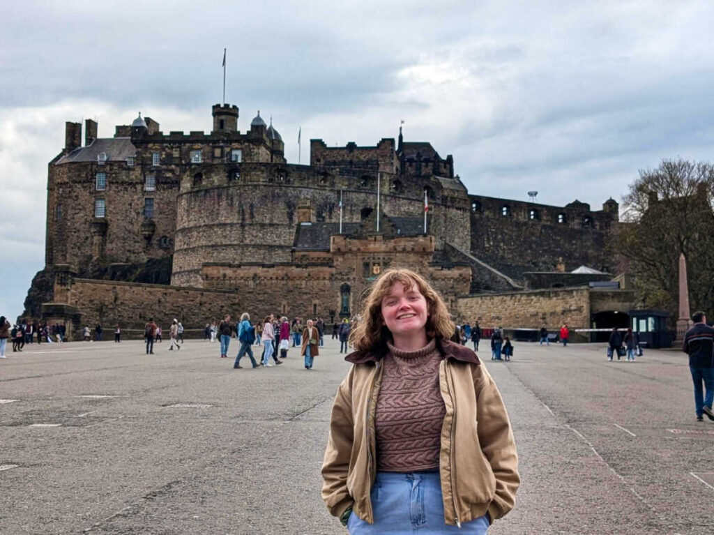 The author Louise Wylie, posing for a photo with a panoramic view of the Edinburgh Castle Esplanade