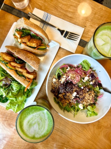 A plate of vegetable sandwich and salad with two glasses of matcha lattes