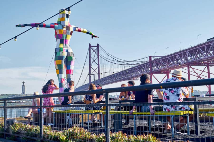 People enjoying at the rooftop bar with a huge colorful female sculpture and the bridge at the background