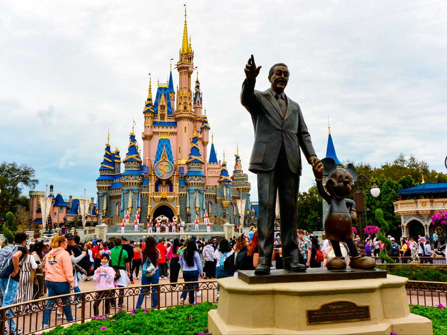 View of people in Disney World and a statue of Walt Disney holding Mickey Mouse