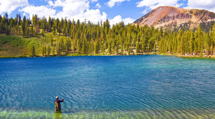 A man fishing at the lake with a picturesque view of the mountain.