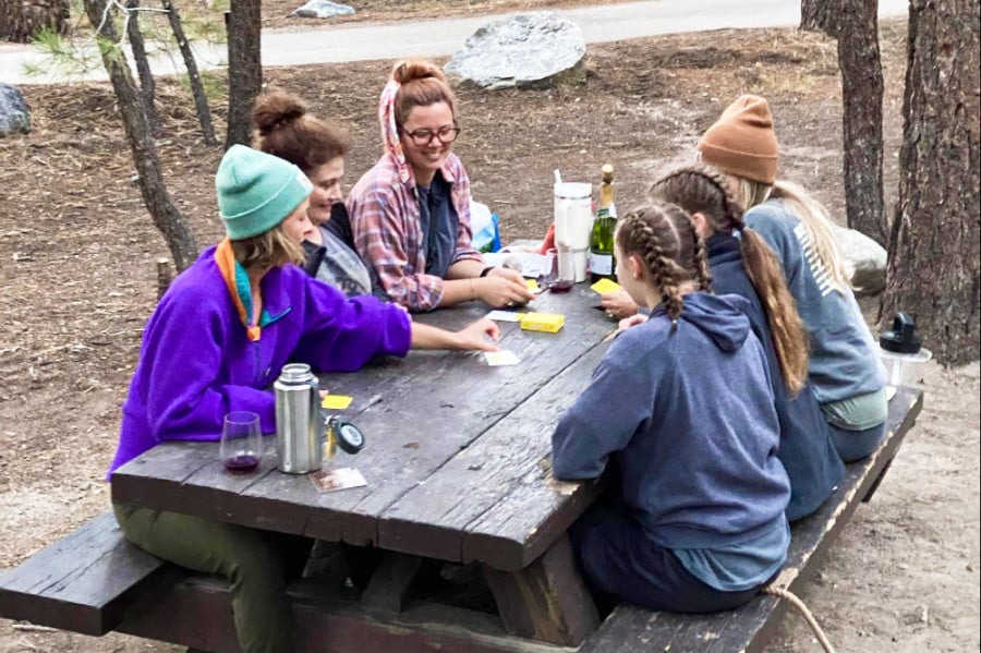 A group of friends playing cards around the table at the campsite.