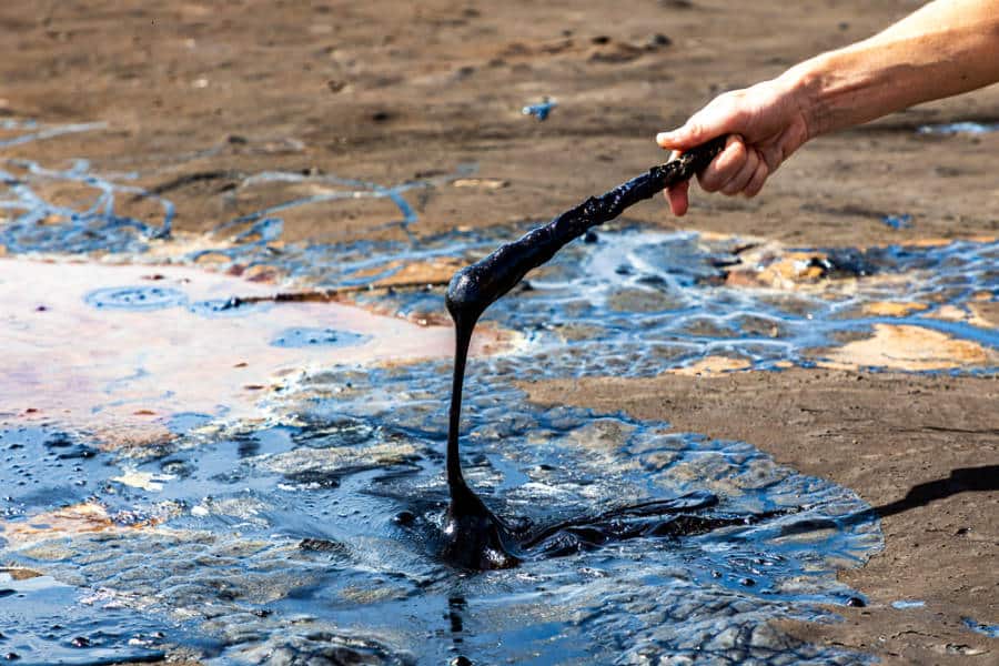 A man's hand holding a stick with liquid asphalt