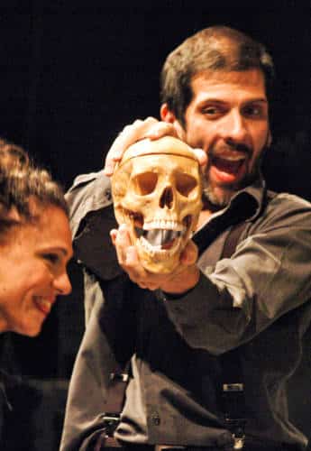 A man holding a skeleton head with a woman on the side during a theater play
