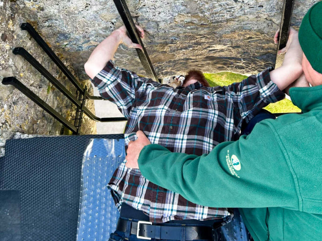 A man helping the author's husband kissing the Blarney Stone