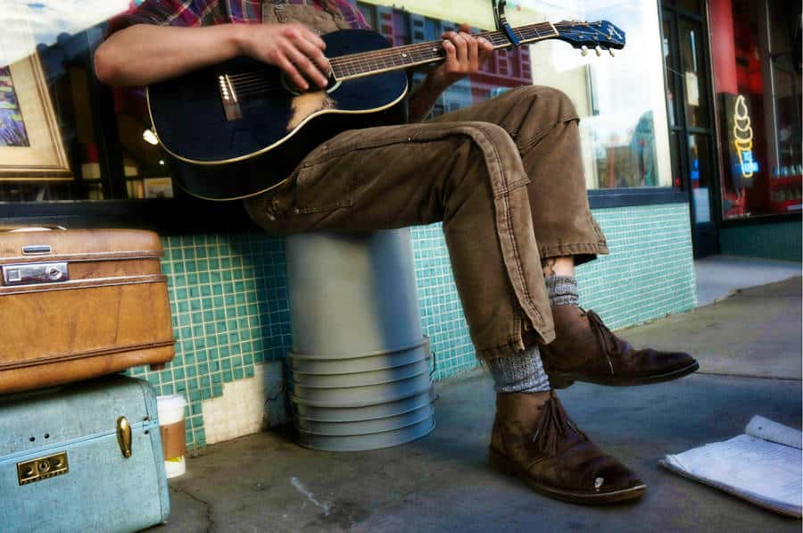 View of a man's feet and hands playing guitar on the street