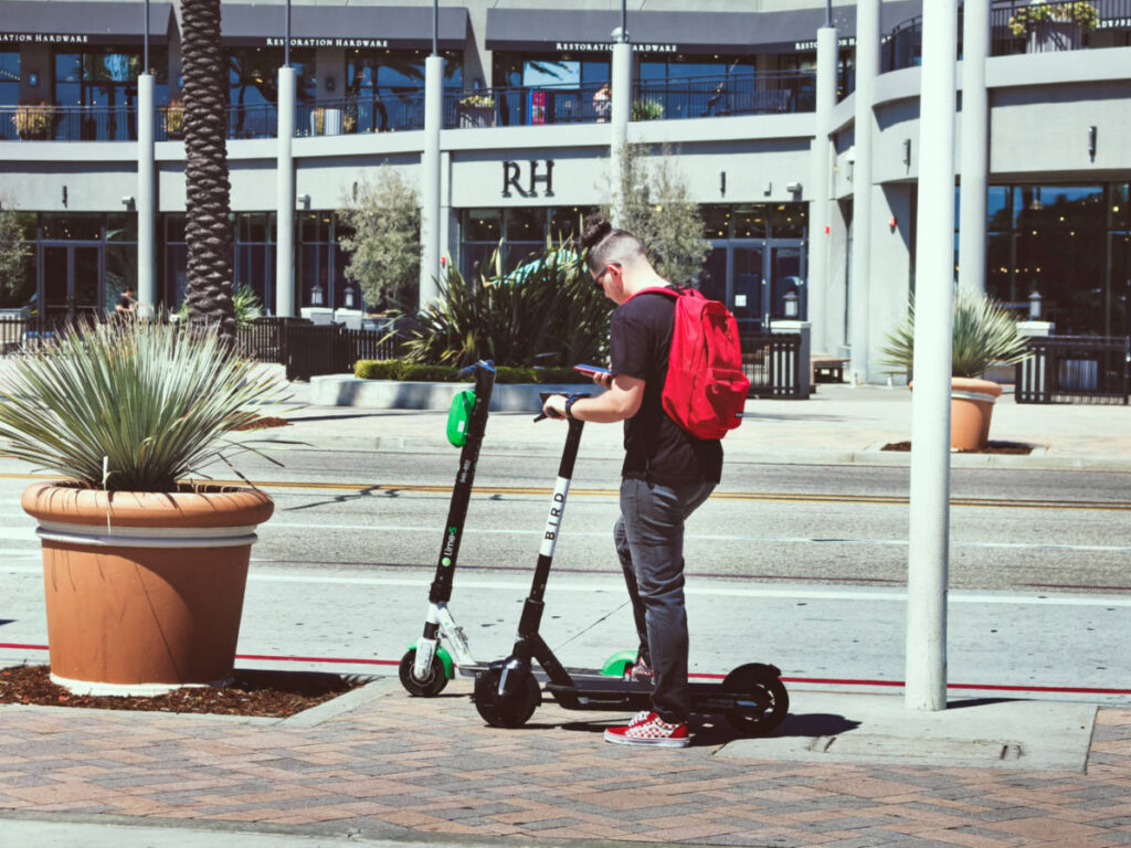 A man holding a cellphone beside the two scooters in Long Beach