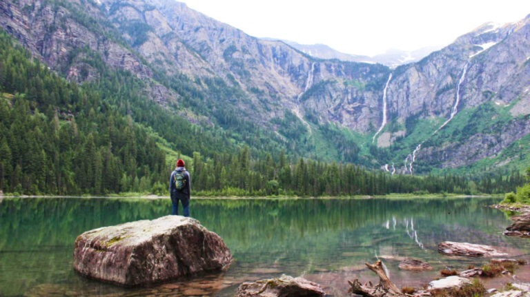 A man standing on a huge rock at the Avalanche Lake surrounded by mountain views
