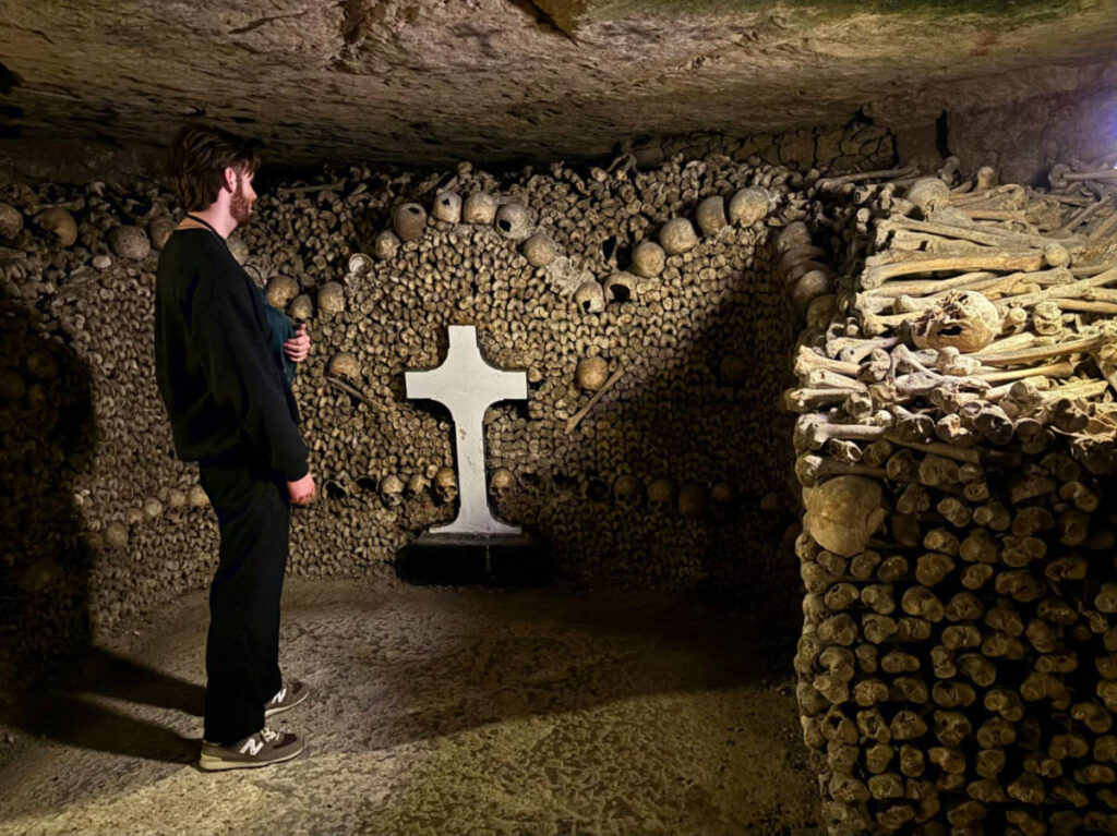 A man looking at the cross and bone constructions within the catacombs of Paris