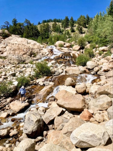 A man walking down the rocky Alluvial Fan Trail near a river