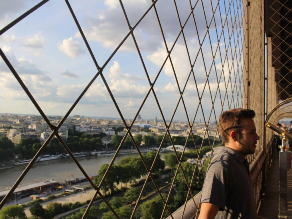 Man leaning the fence withy an overlooking view of the Paris skyline from the Eiffel Tower