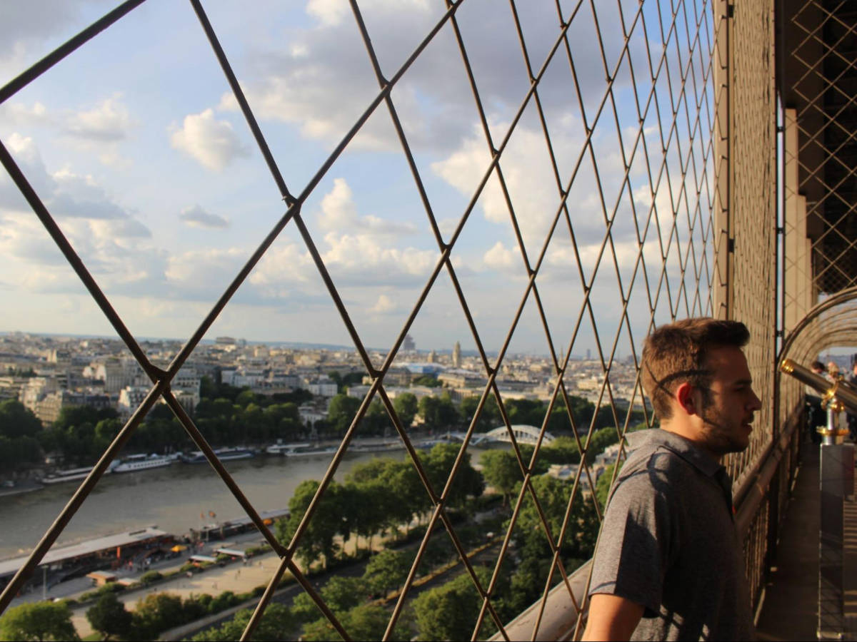 Man leaning the fence withy an overlooking view of the Paris skyline from the Eiffel Tower