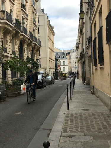 A man cycling down a narrow Marais street