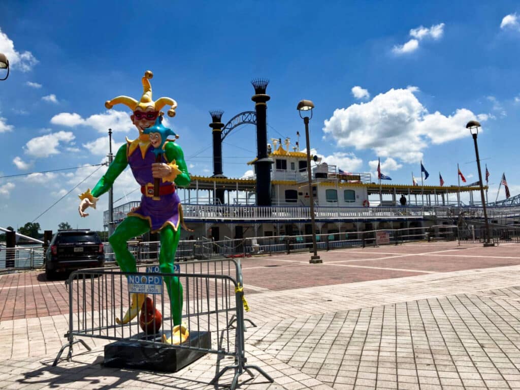 A statue of the Mardi Gras jester near the river on a sunny day
