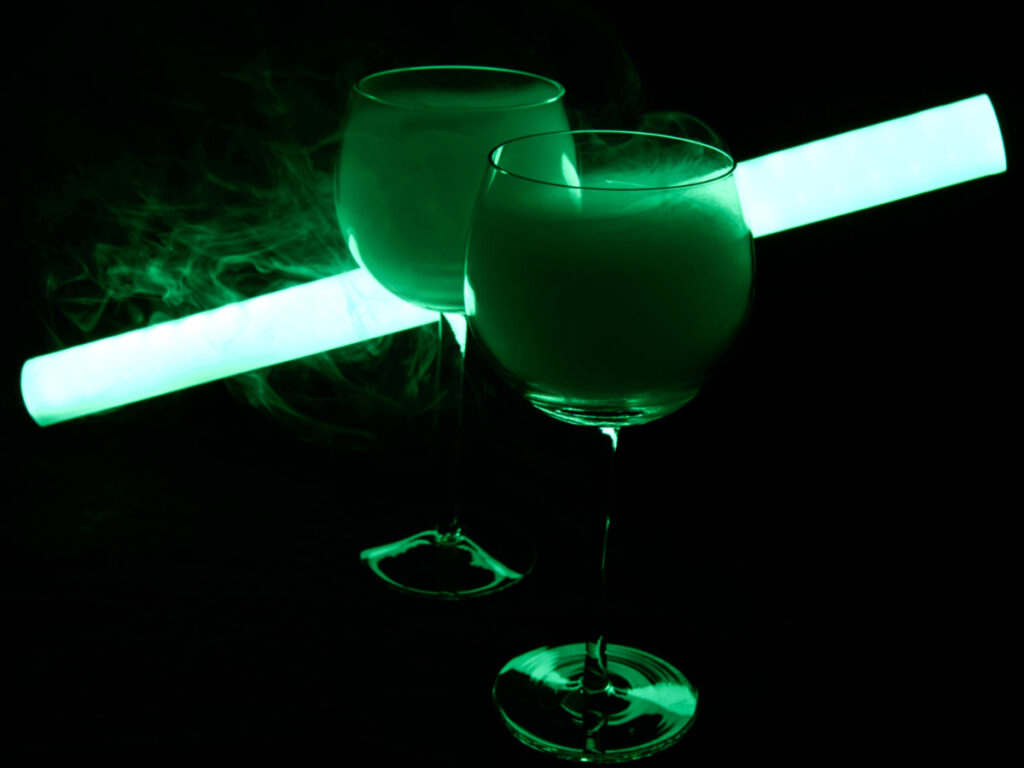 Two glasses of martini cocktail with a green neon light in a dark room