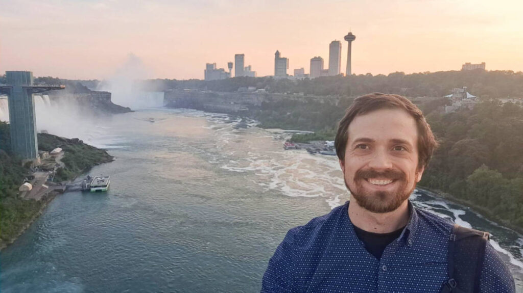 The author Matthew Reppond smiling for a photo with the Niagara Falls on his background
