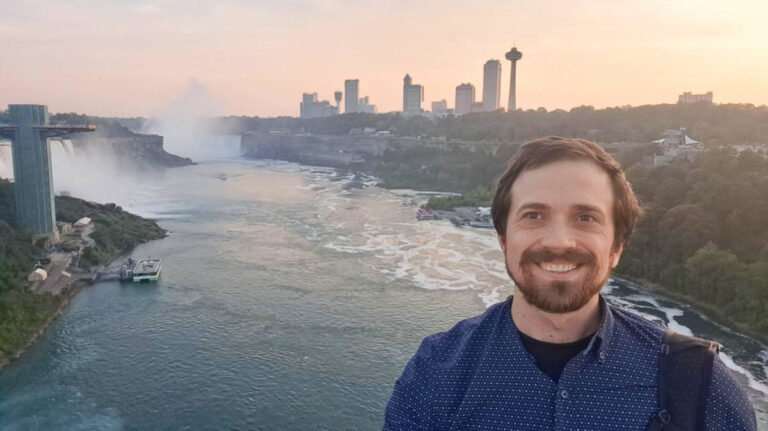 The author Matthew Reppond smiling for a photo with the Niagara Falls on his background