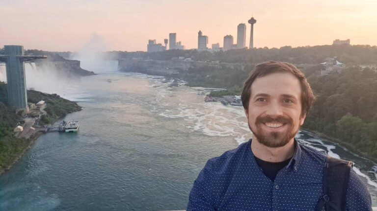 The author Matthew Reppond smiling for a photo with the Niagara Falls on his background
