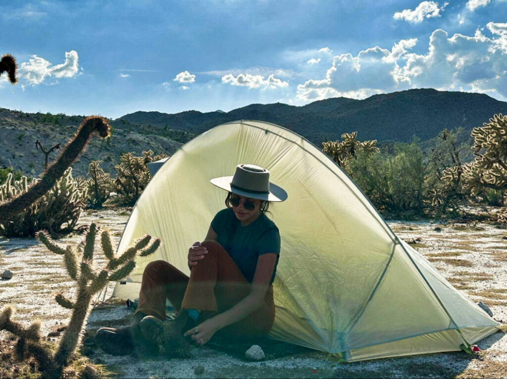 The author Mckenna Mobley, sitting in front of her tent with cholla cacti in Anza Borrego Desert State Park