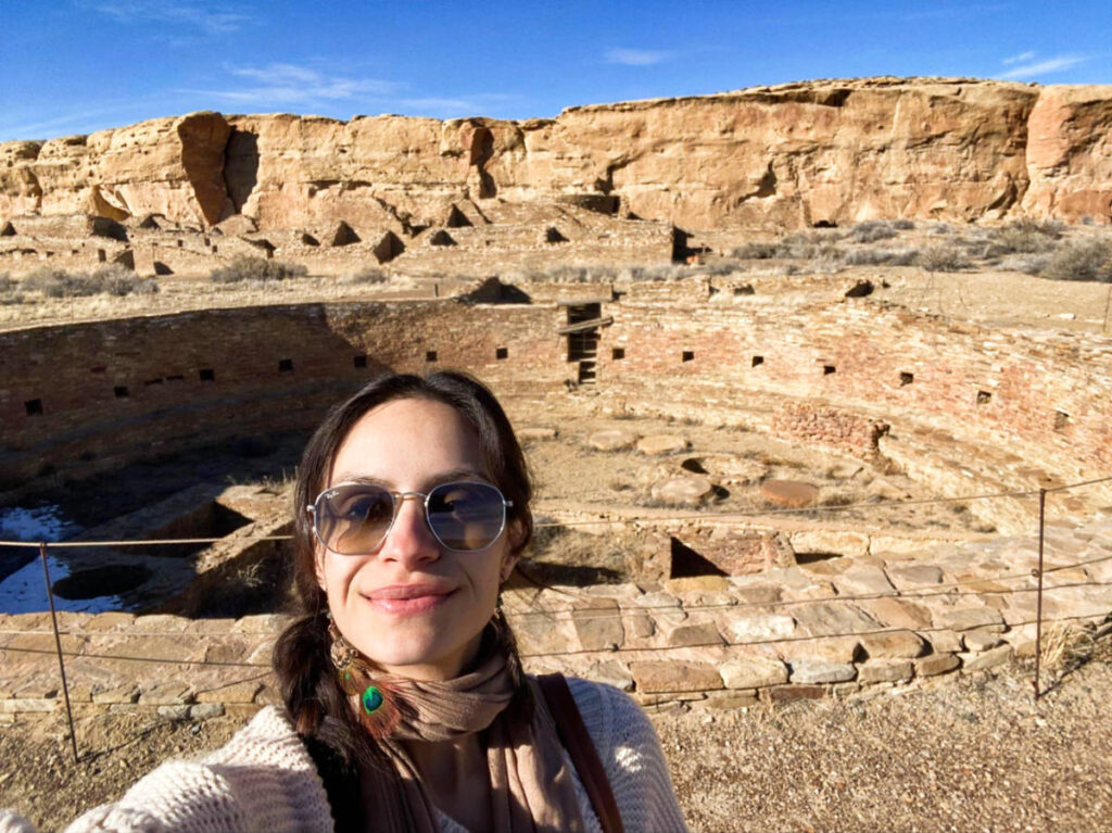 The author Mckenna Mobley, posing in front of the Chetro Ketl Chacoan Great House on a sunny day