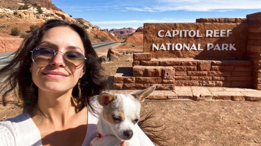 The author McKenna Mobley with her dog posing at the Capitol Reef National Park entrance sign