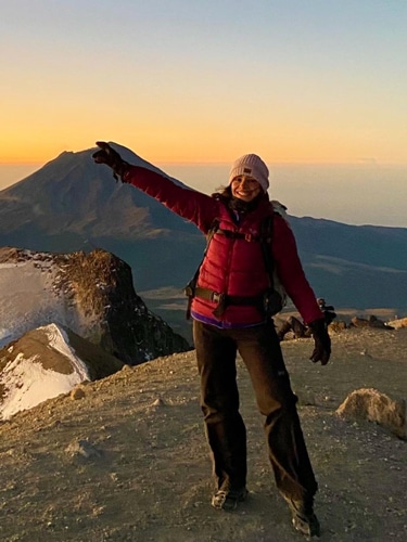 The author McKenna Mobley posing at the summit of Iztaccihuatl with the famous Popocatepetl Volcano in the background during sunset