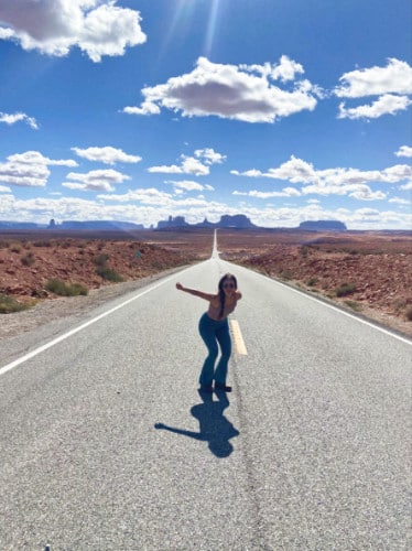 The author McKenna posing in the middle of the road with the Monument Valley towers in her background