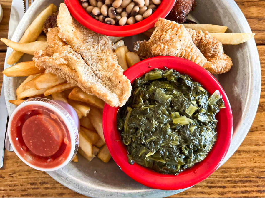 A plate of fries with fried catfish, beans, vegetable and sauce on top