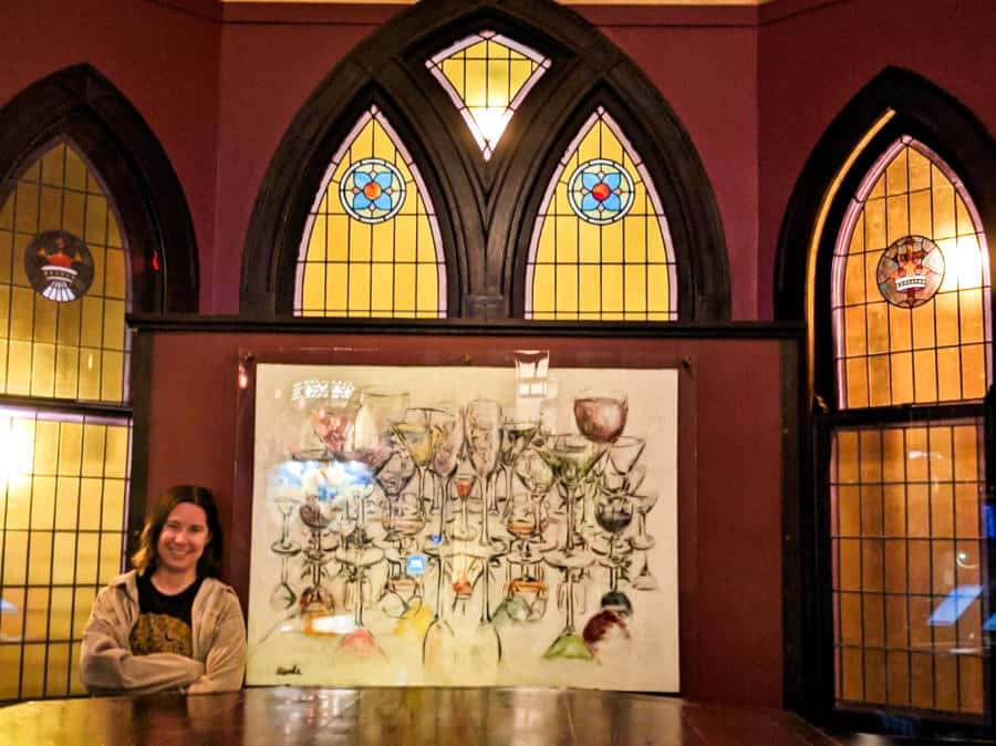 The author Meg O'Connor posing inside the bar Vessel with tall stained glass windows in the background
