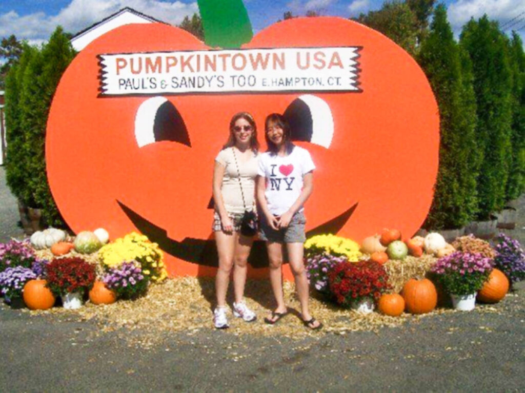 The author Meg O'Connor, posing for a photo with a friend at the huge pumpkin sign surrounded with flowers at Pumpkintown USA