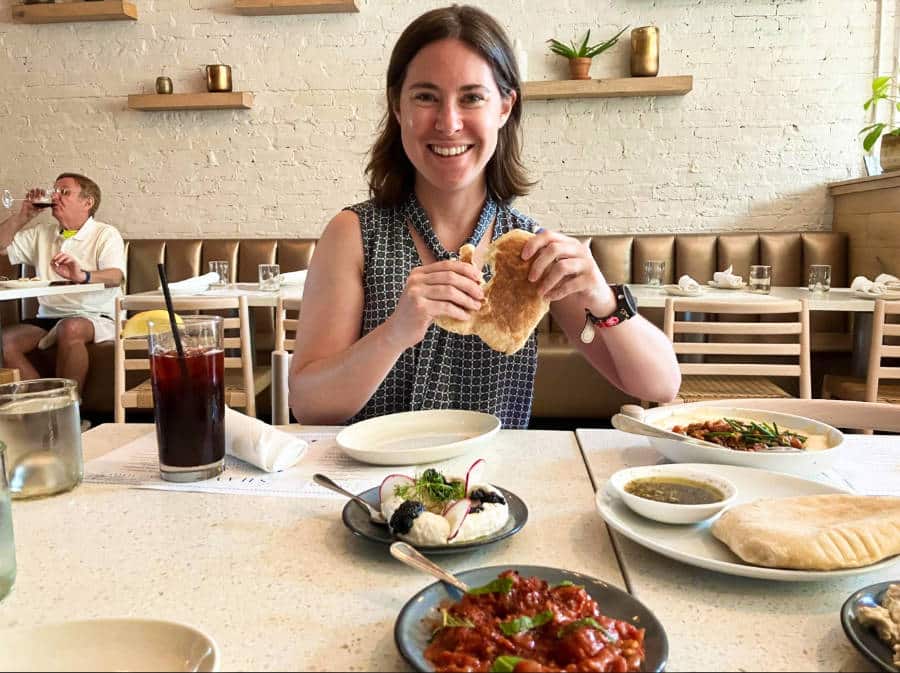 The author, Meg, holding a pita bread with other dishes on the table at Shaya Restaurant