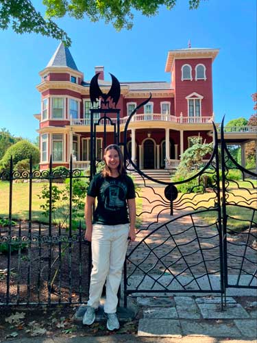 Meg O’Connor smiling for a photo with the Stephen King’s house on her background