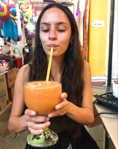 The author McKenna Mobley drinking a huge glass of papaya, mango, and pineapple smoothie inside the market