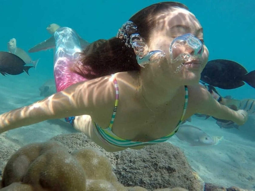 A girl swimming under the water with a mermaid tail