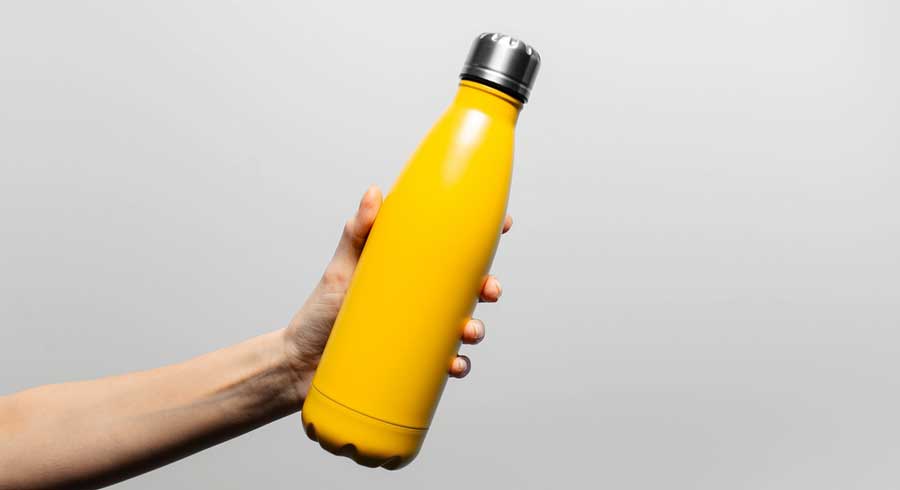 A hand holding a yellow metal reusable water bottle