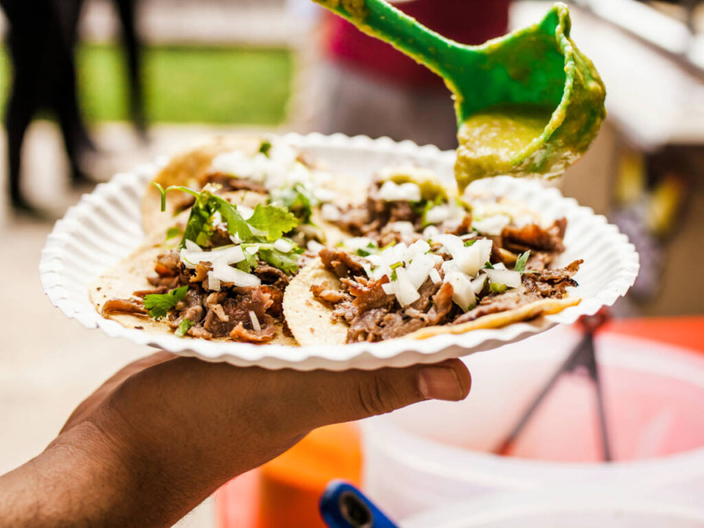 A hand pouring the sauce to the plate with tacos with beef