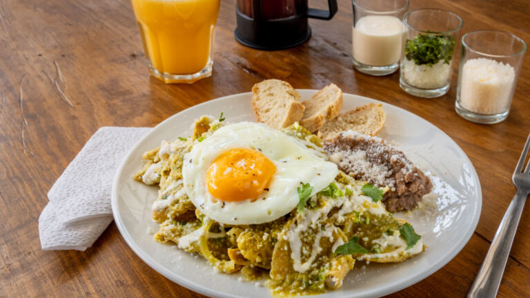 Mexican traditional chilaquiles breakfast with orange juice and coffee placed in a wooden table
