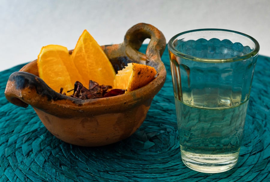 A glass of Mezcal beverage and a small bowl of sliced oranges