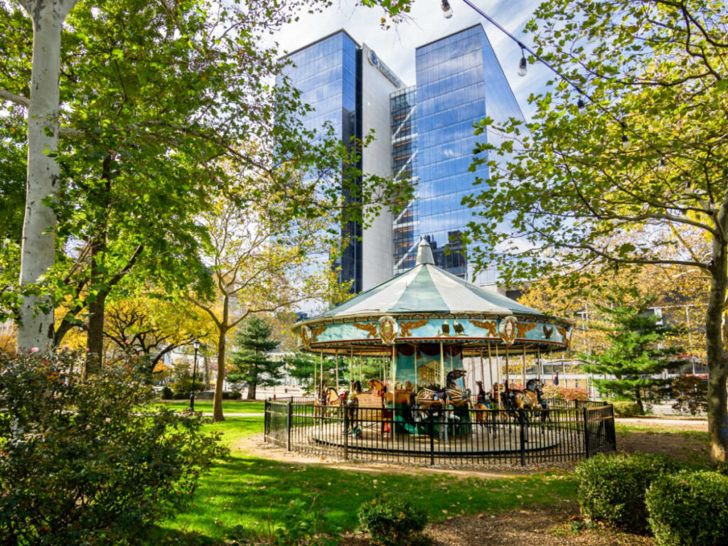A carousel surrounded by greenery in the Military Park with the buildings in the background
